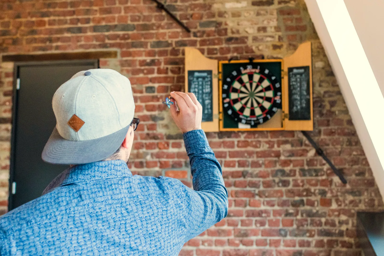 A player lining up a dart throw at a wall-mounted dartboard